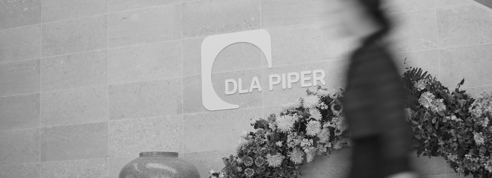 Coworker walking past wall with DLA Piper logo